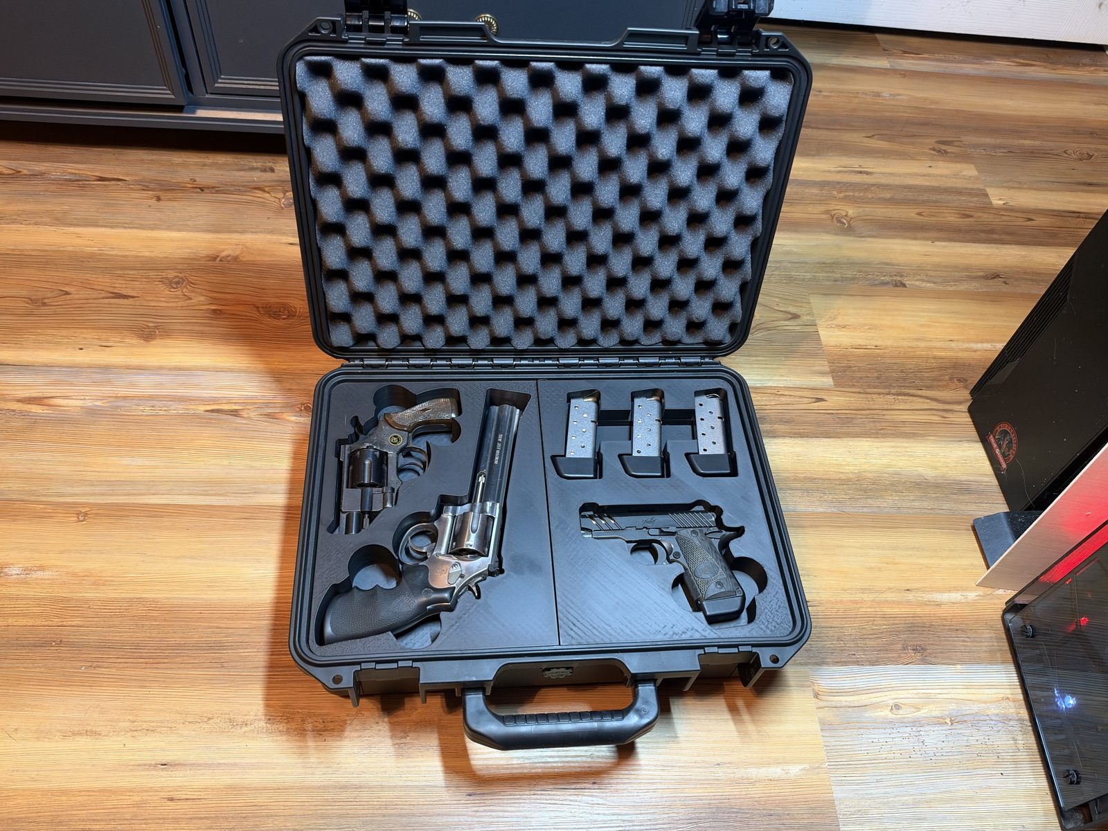 An open hard gun case with a printed insert holding two revolvers, a compact pistol and three magazines.