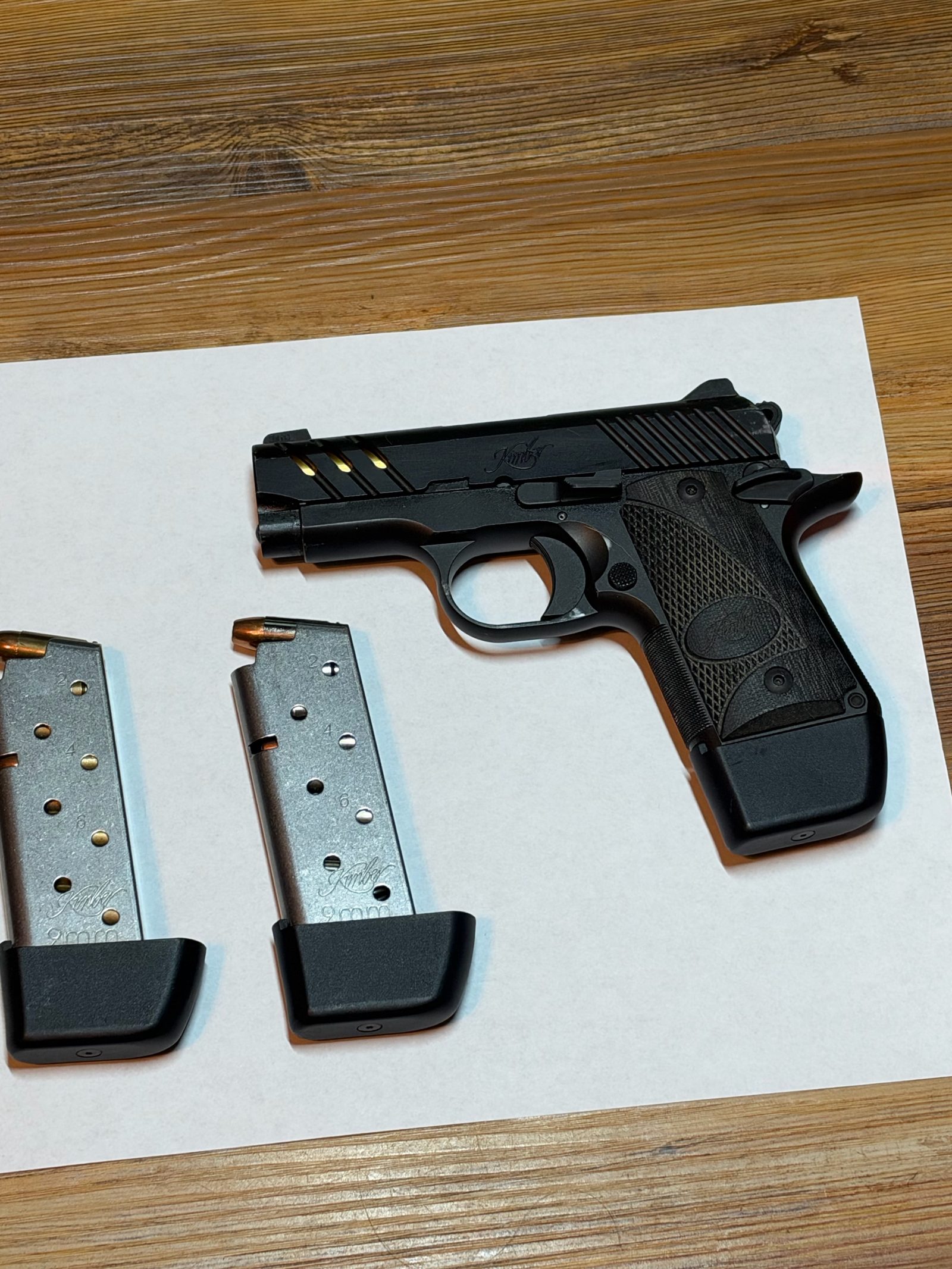 A gun and magazines on printer paper, shot at an angle with a corner of the sheet cut off.
