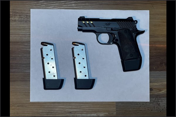 A pistol and two magazines on a blank sheet of printer paper, shot from directly overhead.