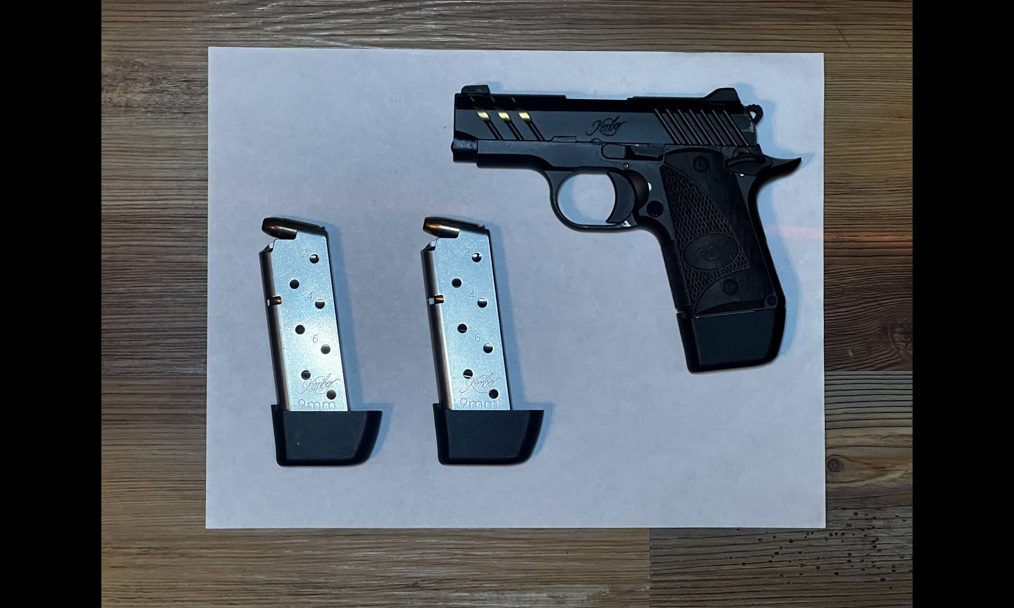 A gun and magazines on a blank sheet of printer paper, shot from directly overhead.